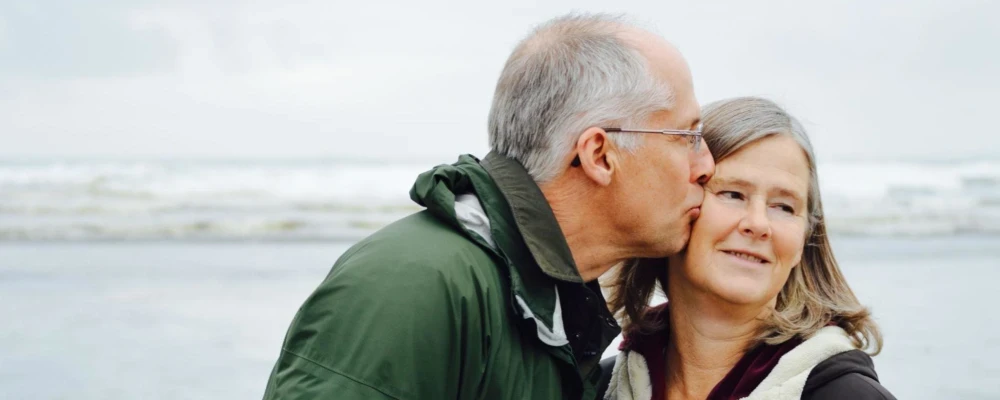 An elderly man kissing the cheek of an elderly woman on the beach