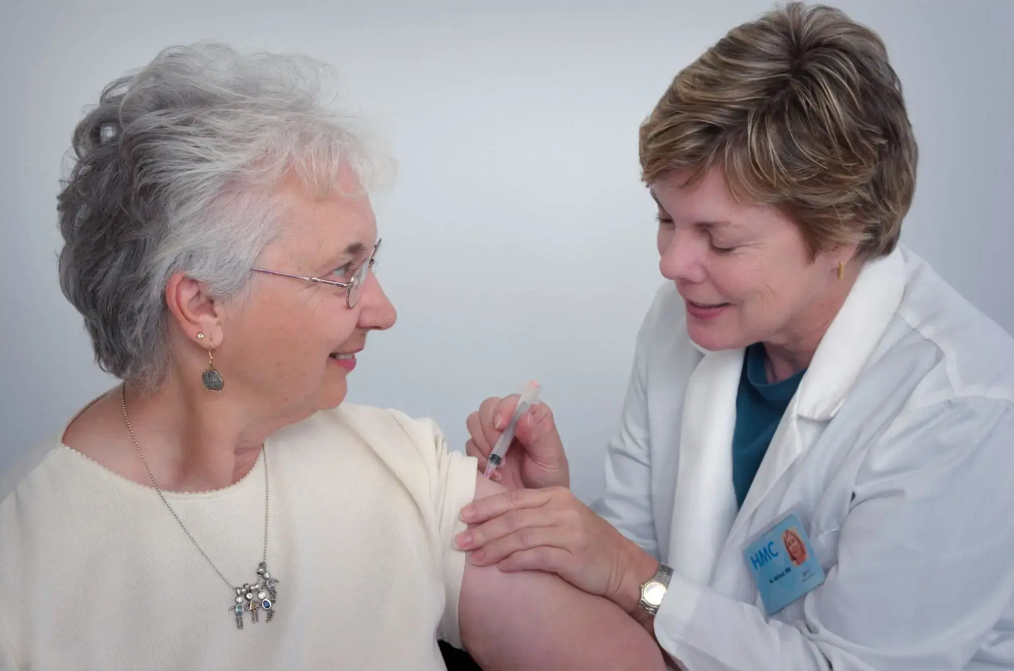 An elderly woman getting shots from a nurse that are covered by her HMO Plan.