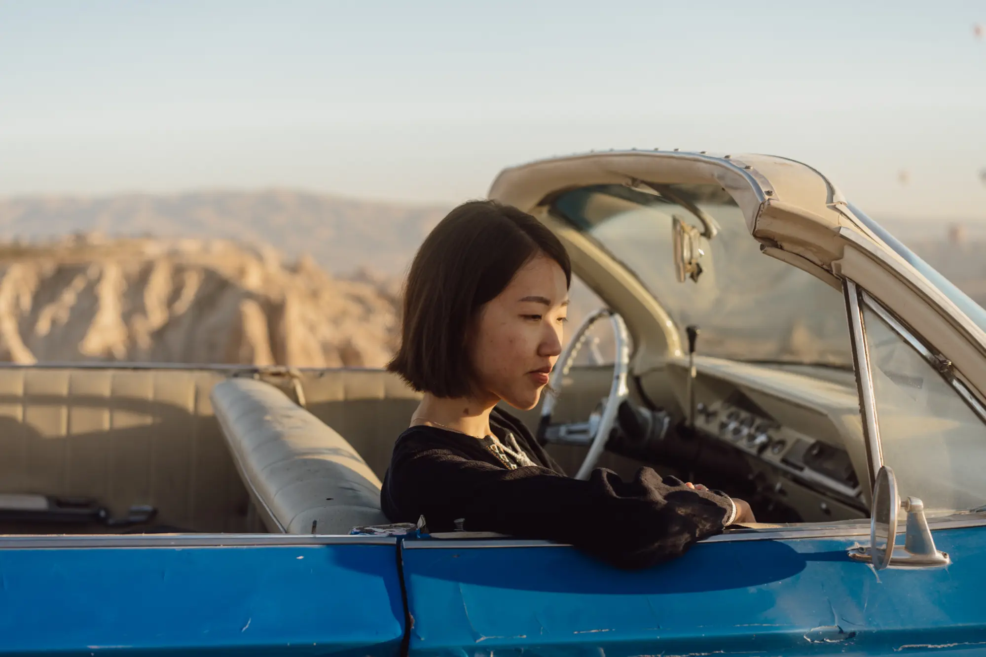 woman sitting in convertible car with mountain range background