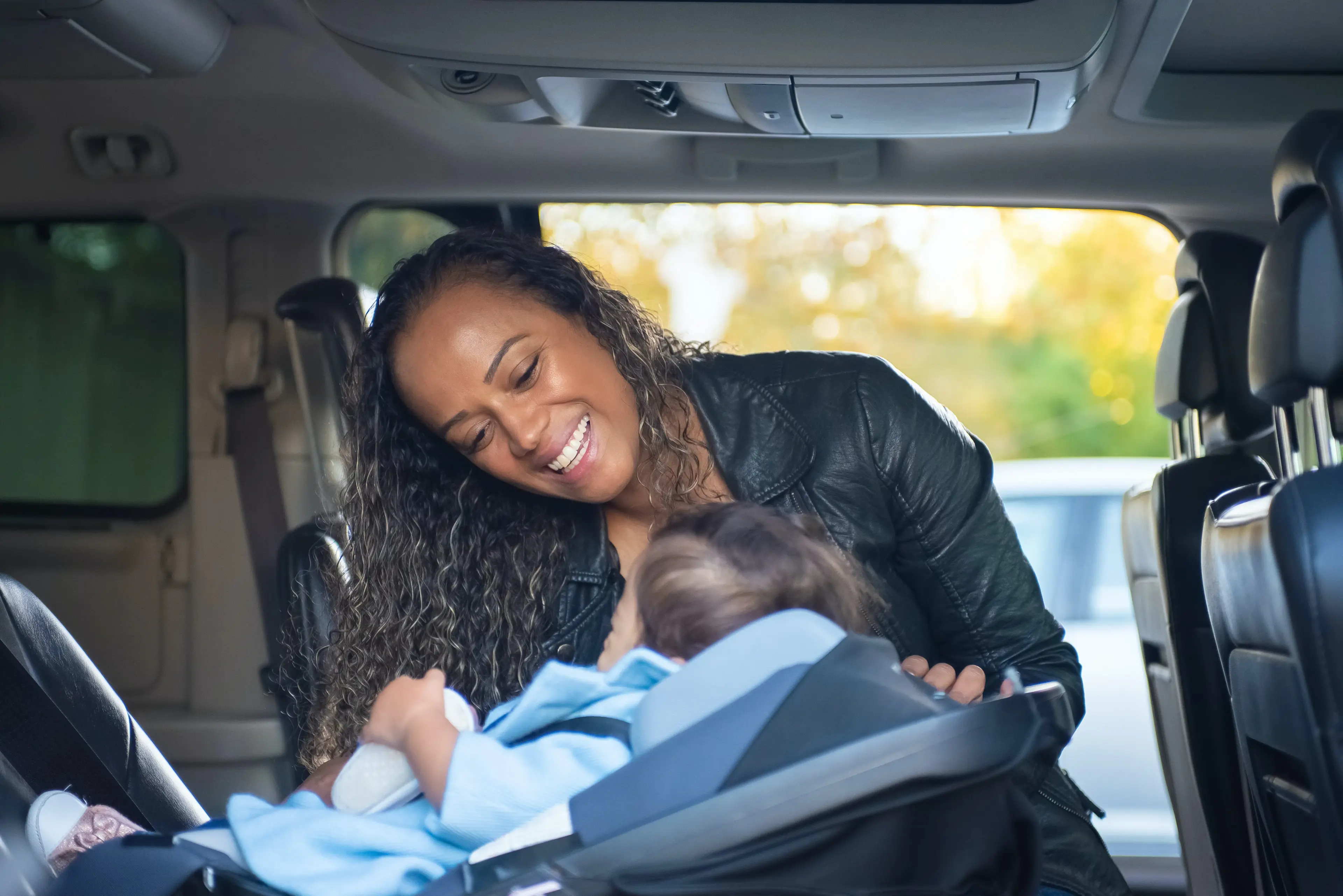 Woman in Black Leather Jacket Tending To Child Sitting on Car Seat