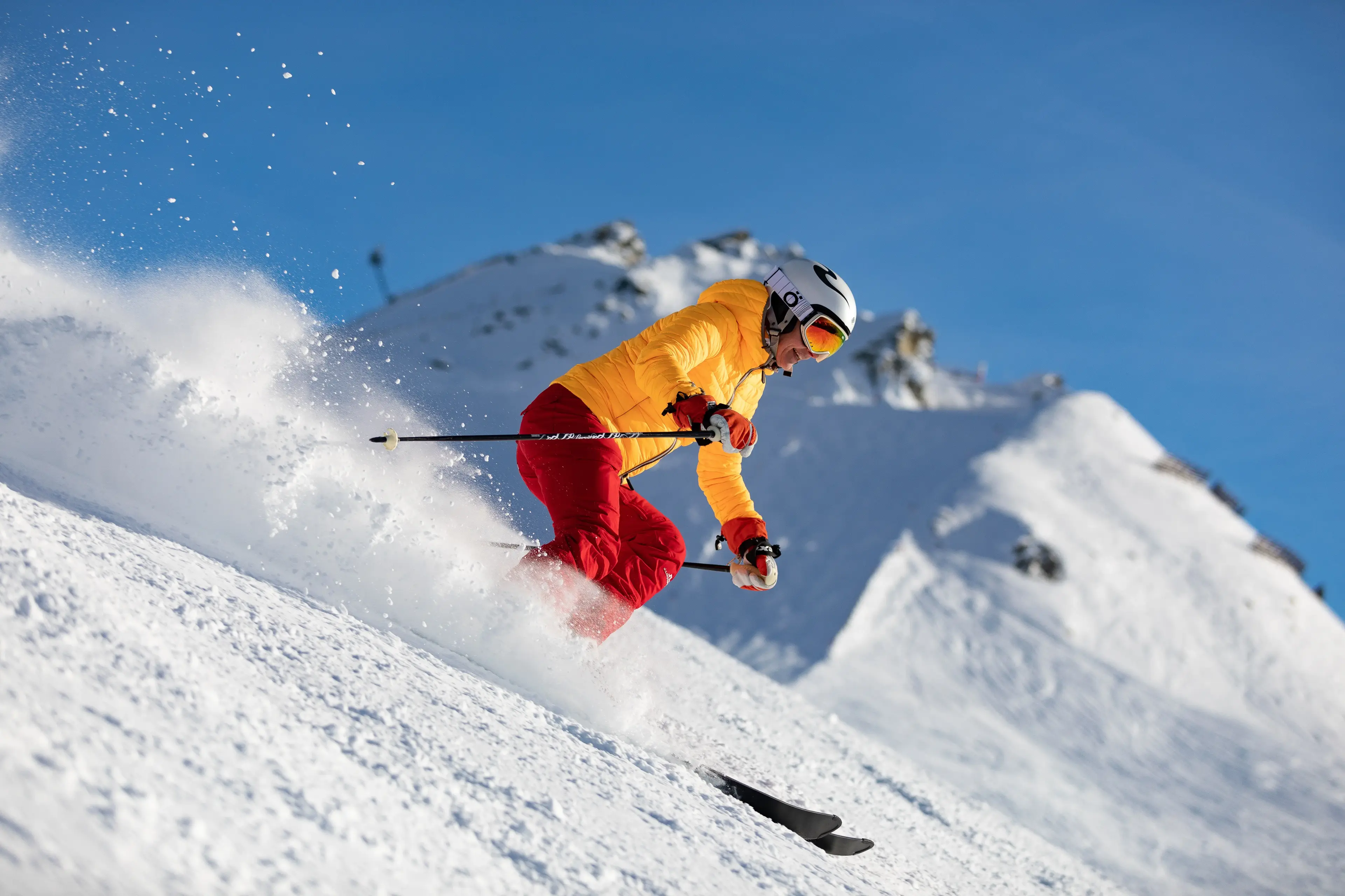 Person in yellow jacket and red pants skiing down mountain